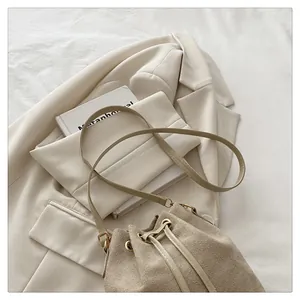 Close-up of beige suede drawstring bucket bag with gold hardware on a neutral suit