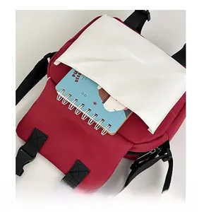 Detail view of red canvas crossbody bag front pocket with buckle and notebook storage