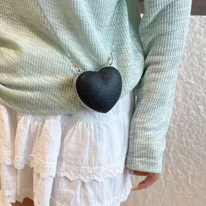 Sac bandoulière noir brillant en forme de cœur avec une fine chaîne en métal argenté