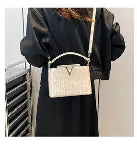 Detail of cream crocodile embossed handbag featuring a gold V-shaped metal clasp and strap