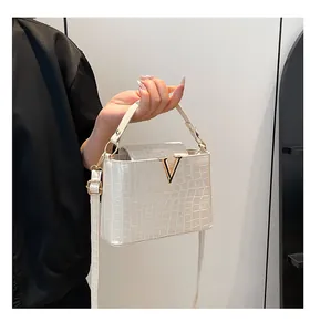 Detail of off-white crocodile embossed leather handbag with golden V-shaped metal clasp