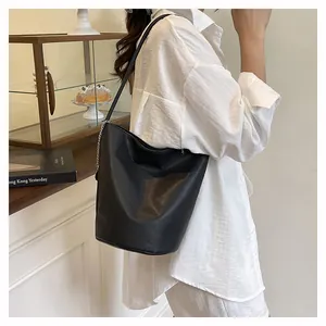 Side view of black pebble leather bucket bag with silver chain detail on female model