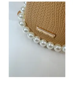 Detail of khaki woven bucket bag featuring large pearl strap and gold metal clasp closure