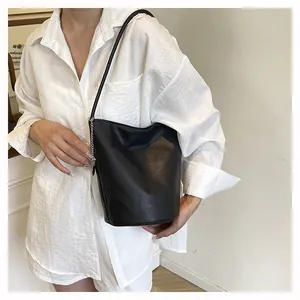 Detail of black pebbled leather bucket bag with slim shoulder strap and chain accent