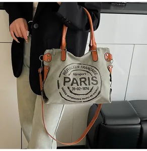 Detail of grey canvas tote bag with brown leather straps worn by model in casual style