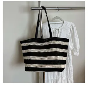 Vista detallada del bolso tote tejido a rayas con textura de malla y asas de cuero negro