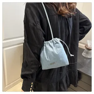 Detail of light blue denim bucket bag with drawstring closure and silver logo accent