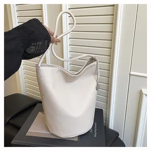 Detail of off-white leather bucket bag with cylindrical handle and silver chain ornament