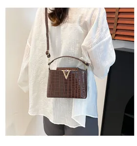 Detail of dark brown crocodile embossed leather bag with golden V-shaped metal buckle clasp