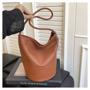 Detail view of brown pebbled leather bucket bag with silver chain and metal charm