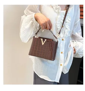 Detail of dark brown crocodile embossed leather bag with gold V-shaped metal buckle