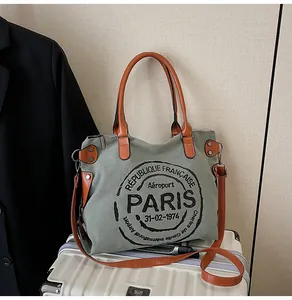 Detail of vintage grey canvas tote bag with brown handles placed on white luggage case