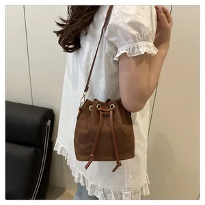 Close-up of brown suede bucket bag with drawstring closure and gold hardware details