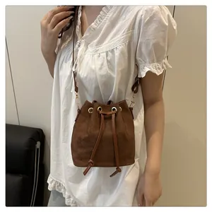 Detail of dark brown matte suede bucket bag with gold eyelets and crossbody strap