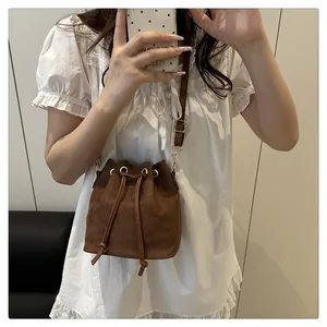 Detailed close-up of dark brown suede bucket bag with drawstring and golden eyelets