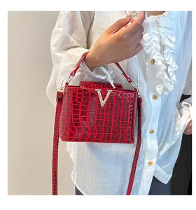 Detailed view of red crocodile-embossed handbag with gold V-shaped metal hardware