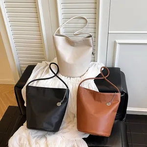 Three minimalist soft leather bucket bags in beige, black, and brown with chain charms