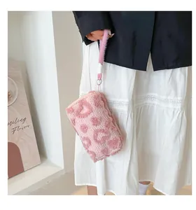 Detail of soft pink plush makeup bag with embossed heart pattern and fuzzy wrist strap