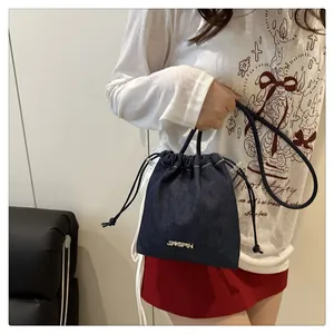 Detail of dark blue denim drawstring bucket bag with metallic logo on textured fabric