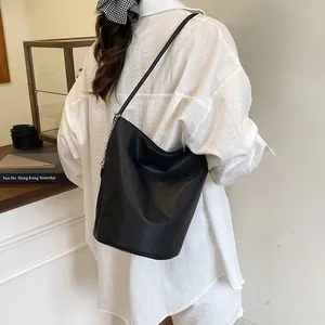 Minimalist black leather bucket bag with chain-linked shoulder strap on model
