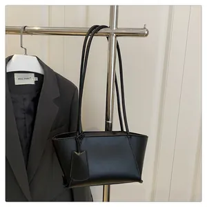 Detail of minimalist black faux leather tote bag hanging next to a grey blazer