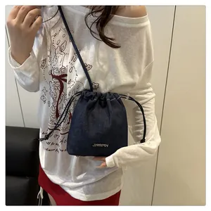 Detail of blue denim mini bucket bag featuring metal logo and white drawstring closure