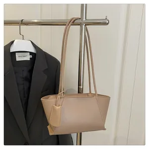 Detail of a beige leather tote bag with slim shoulder straps and hanging tag accessory