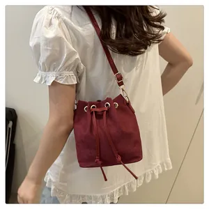 Detail of burgundy bucket bag featuring drawstring closure and gold hardware on model