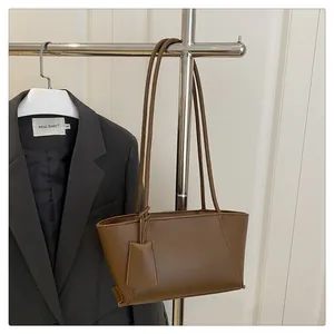 Detail of a brown faux leather tote bag with slim shoulder straps on a metal stand