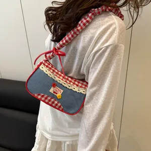 Denim underarm bag with red gingham trim, lace edges and a cherry patch on a model