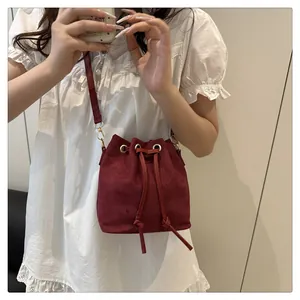Detail of burgundy bucket bag with drawstring closure and golden hardware finish