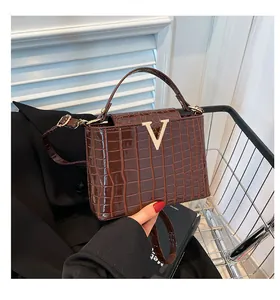 Detail view of brown crocodile texture leather bag with large golden metal V-buckle closure