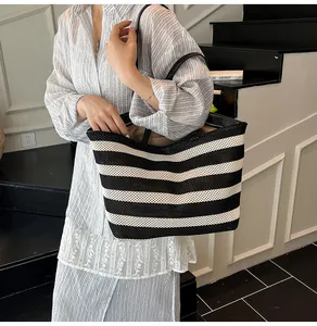 Detalle del bolso tote de tejido a rayas con asas finas de cuero negro y cremallera