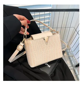 Detail view of beige crocodile embossed handbag with gold V buckle on a metal cart