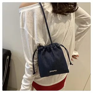 Detail of blue denim bucket bag with drawstring closure and metal logo shown on model