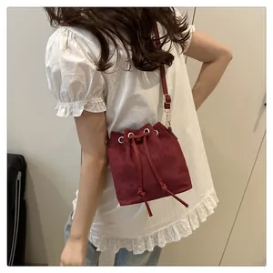 Detail of burgundy bucket bag with drawstring closure and rivet accents on a model