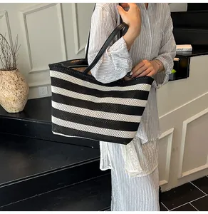 Detalle de bolso tote tejido a rayas blancas y negras con asas de cuero en ambiente moderno