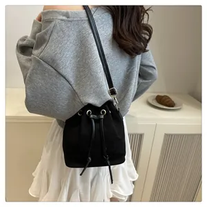 Close-up of black drawstring bucket bag in textured canvas worn cross-body by a model