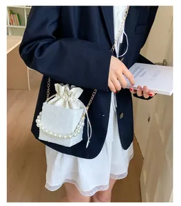 White textured bucket bag with pearl handle and golden chain strap on a model