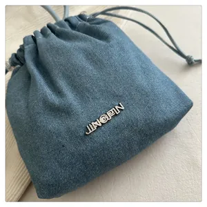 Close-up of blue denim drawstring bucket bag with silver metal logo on textured background