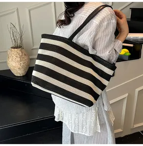 Vista detallada de un bolso tote tejido a rayas de gran capacidad en el hombro de modelo