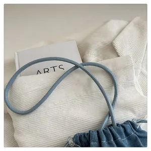 Detail of blue denim bucket bag featuring white stitching and drawstring closure