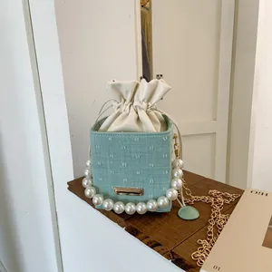 Close-up of light green woven bucket bag with pearl handle and metal chain detail