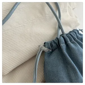Close-up of blue denim bucket bag with drawstring closure and gray leather strap detail