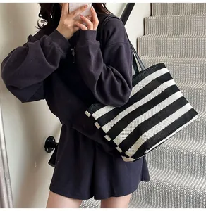 Detalle de un gran bolso tote tejido a rayas blancas y negras con correas negras finas