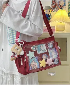 Detail of red ita bag showing transparent PVC window with anime badges and plush pendant