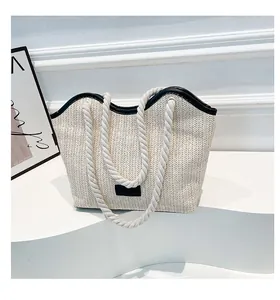 Detailed close-up of woven straw tote bag featuring contrast black leather trim and rope handles
