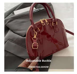 Detalle del bolso de charol burdeos con cremallera dorada y hebilla de ajuste ajustable