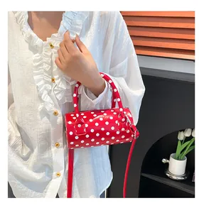 Polished red cylindrical handbag with white polka dots carried by a model in a white blouse