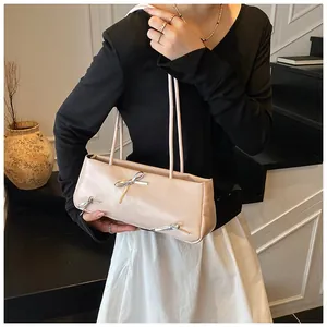 Detail of beige shoulder bag with silver bow accent on a model in a minimalist setting
